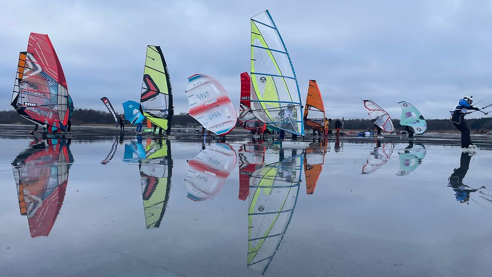 Flera färgglada vindsurfingsegel står uppradade på Hjälmarens istäcke.