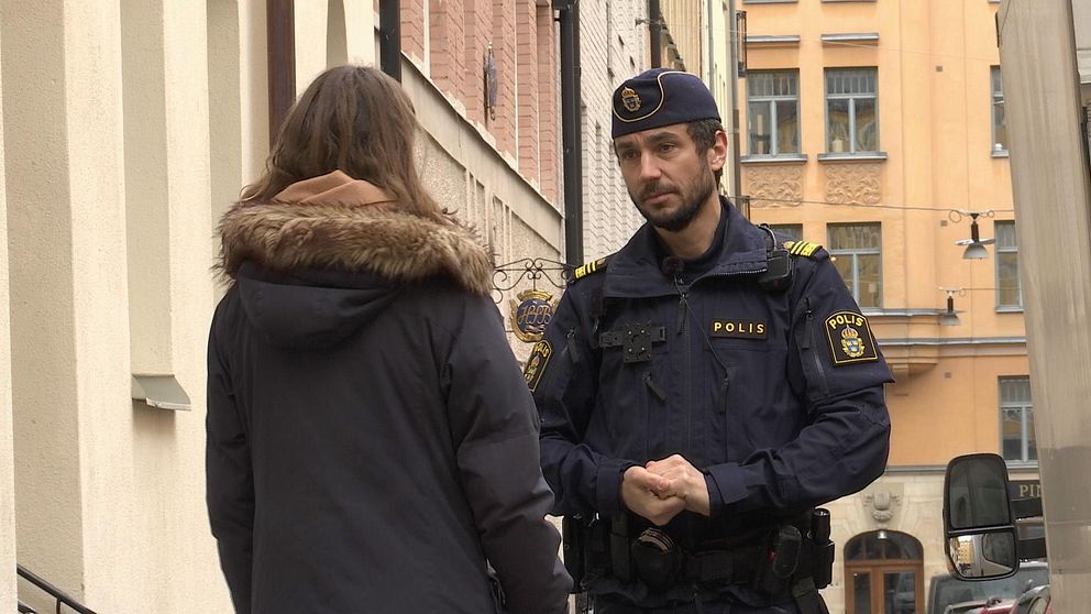 Polis står och pratar med en reporter på en gata.