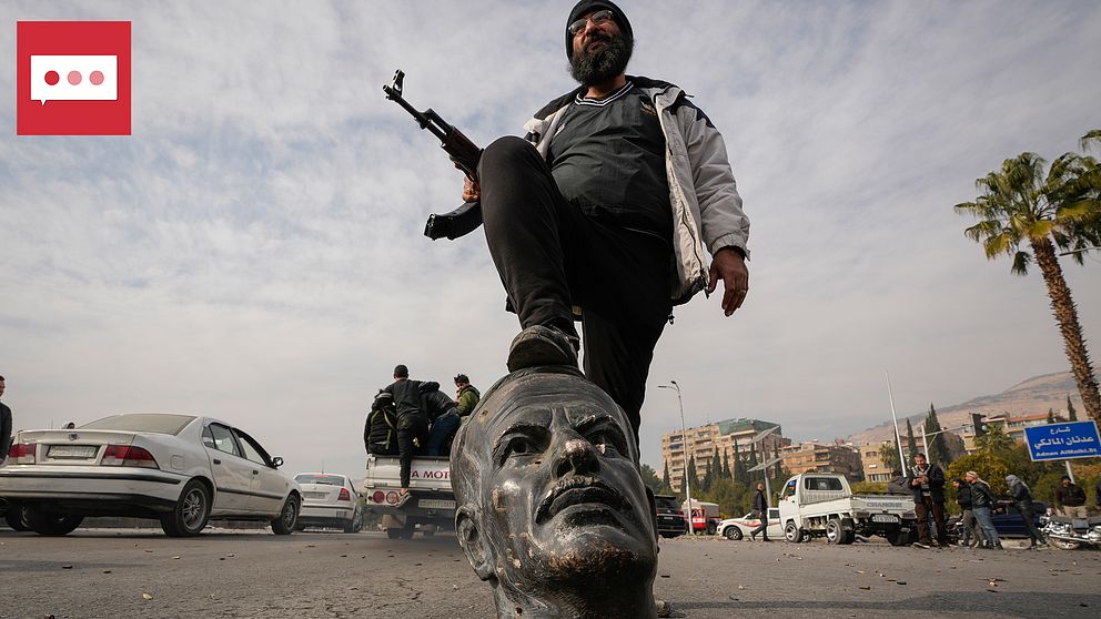 En beväpnad rebell står med ena foten på en skulptur föreställande av den avlidne presidenten Hafez Assad i Damaskus.