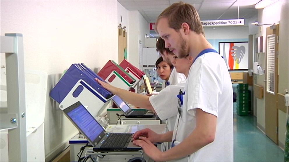 Två vårdanställda arbetar vid datorer i en sjukhuskorridor medan de granskar patientdokumentation.