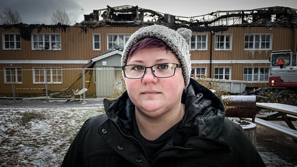 En ung kvinna står framför ett flerfamiljshuset som har brunnit.