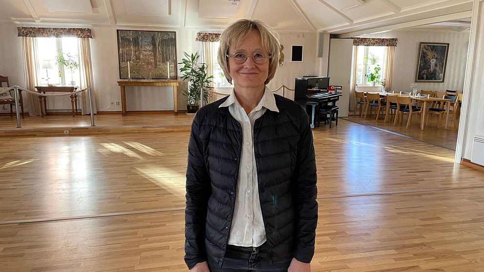 Kvinna med blont hår och glasögon ler mot kameran.