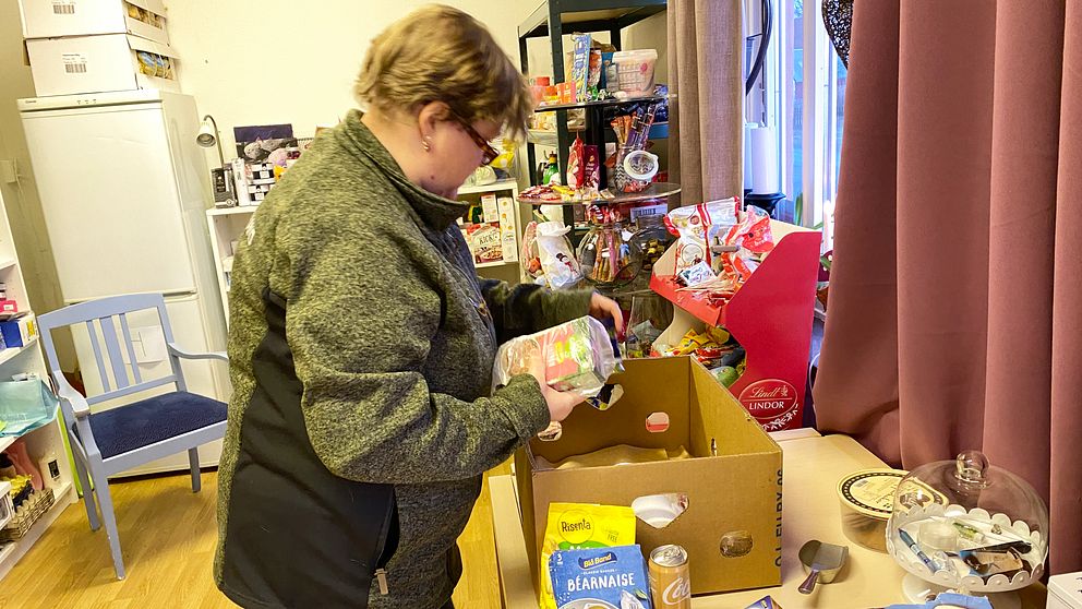 Kvinna framför mathyllor som packar matpaket. Kvinnan heter Gunilla Hellsén och är grundare av föreningen Sträck ut en hand, som driver Matbanken i Mjällby.