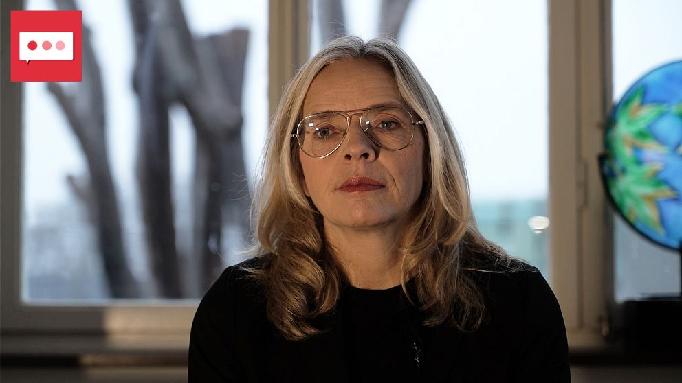En person med ljus hårfärg sitter i förgrunden, framför ett fönster där träd syns i bakgrunden. Till höger finns en färgglad glaskonst. Belysningen skapar en mjuk och dämpad atmosfär.