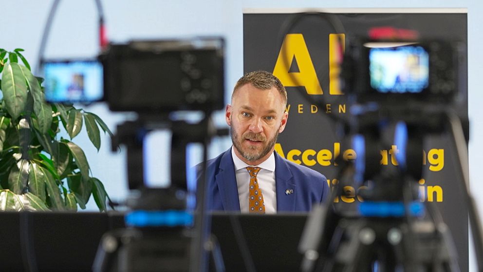 Civilminsiter Erik Slottner bakom flera kameror på en konferens om AI.