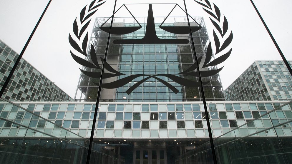 Fasaden av Internationella brottmålsdomstolens byggnad i Haag, med en stor logotyp med vågskål och olivkvistar synlig på glaset.