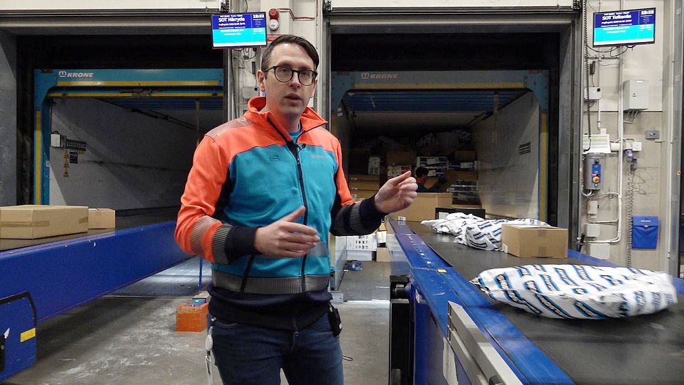 En man med glasögon står vid ett rullband med paket på postterminalen i Växjö.
