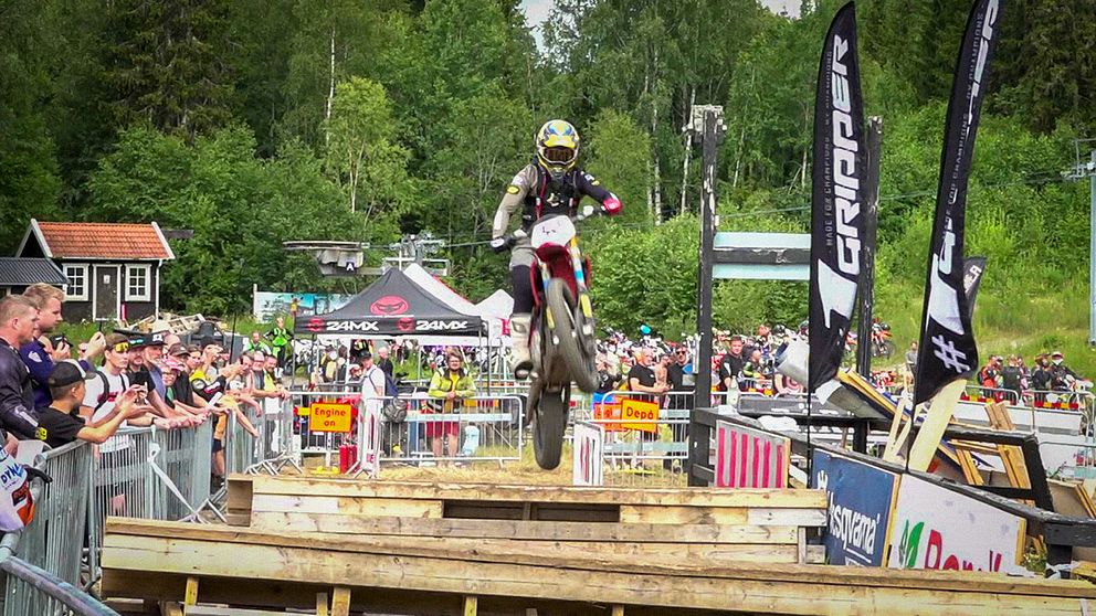 En enduromotorcykel flyger över ett hopp med publik.
