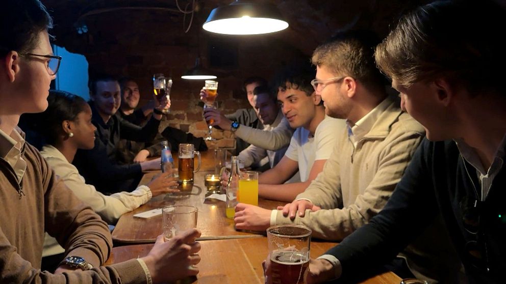 Ett större sällskap skålar och umgås runt ett långbord på en mörk pub.