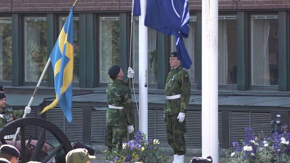 Två män i militärklader hissar en Nato-flagga.