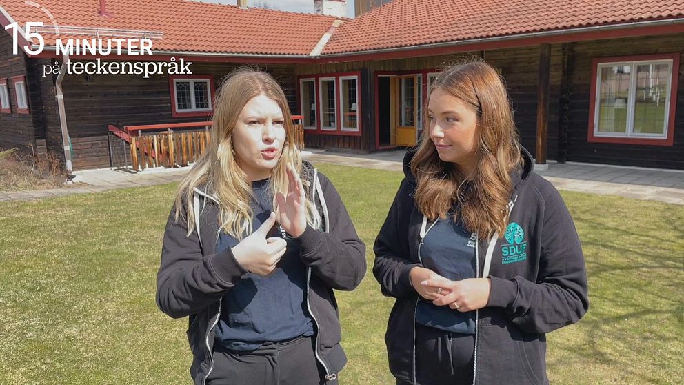 Julia Grahn och Mindie Norrie har på sig svarta kläder och står bredvid varandra på en gräsmatta utanför en skola.