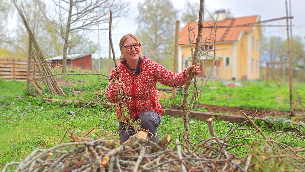 Kvinna står med kvistar och grenar i hand bakom en rishög framför sitt hus i jakt med att välkomna insekter