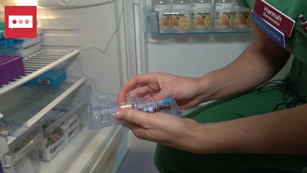Till vänster är ett kylskåp, till höger i bild en persons händer syns hålla i vaccinsprutor. Personen har gröna kläder.