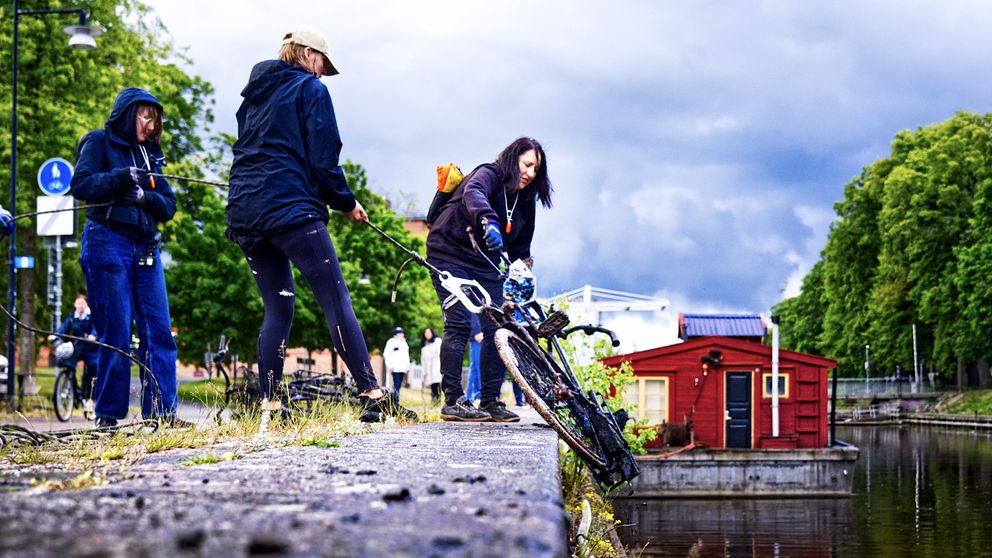 Tre personer som drar i en cykel intill en å