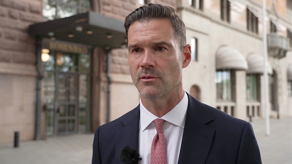 Migrationsministern och moderaten Johan Forssell har en mörk kostym, vit skjorta och ljusröd slips och ler mot kameran.