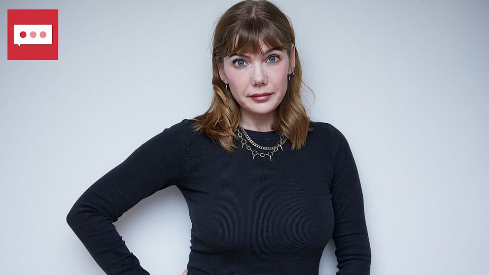 En person, Emily ”Modemassakern” Dahl, står med ena handen på höften, iförd en svart tröja och en kedjesmycke. Bakgrunden är ljus och neutral, vilket skapar fokus på personen. I övre vänstra hörnet finns en röd ikon med pratbubblor.