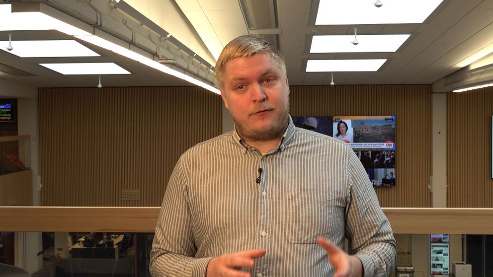 Jimmy Kirvesmäki, reporter på SVT, står talande inomhus med tv-skärmar i bakgrunden.