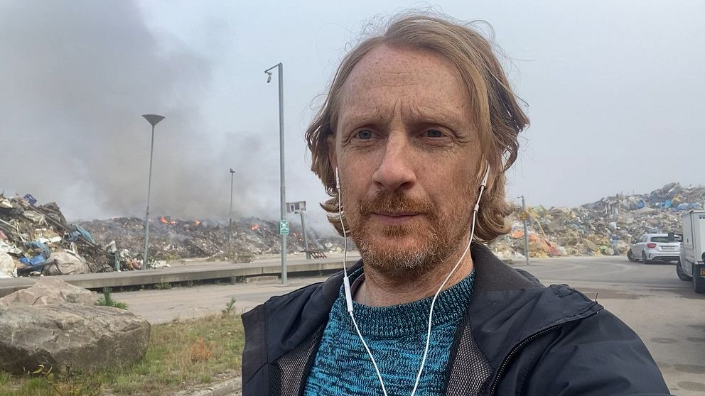 Reporter framför en brinnande avfallshög