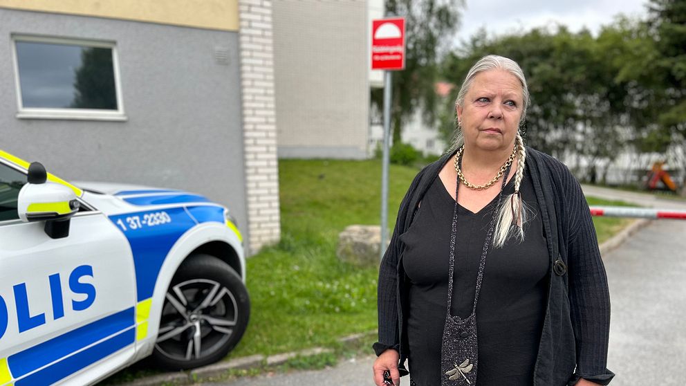 Svartklädd kvinna med håret i en fläta framför polisbil