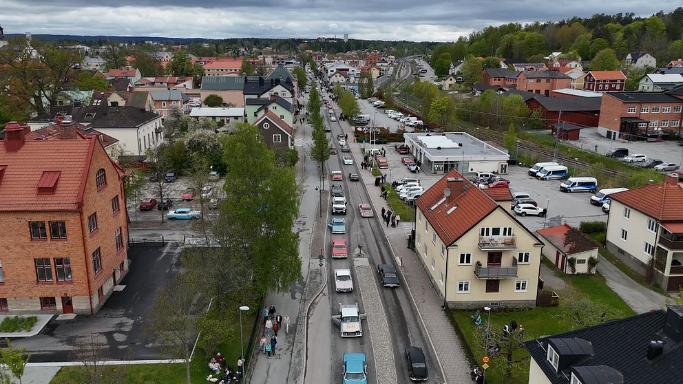 Lång bilkö genom tätort, omgiven av bostadshus och bilar under molnig himmel.
