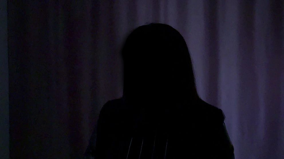 Person i mörker, ansiktet anonymiserat mot bakgrund av ljus gardin.