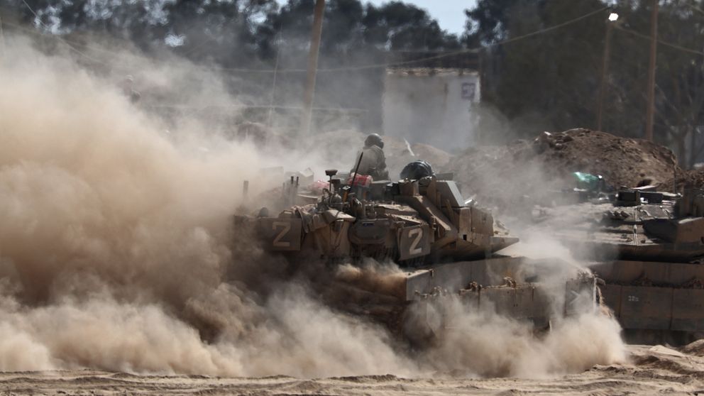 Israelisk stridsvagn vid Gazas gräns omgiven av damm och rök.
