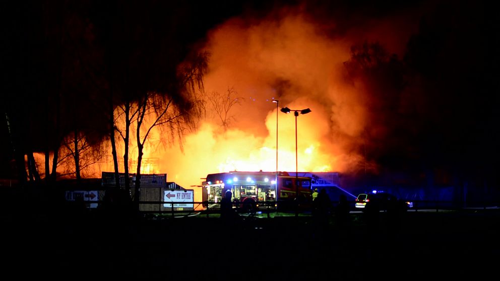 En byggnad står i brand med brandbilar framför.