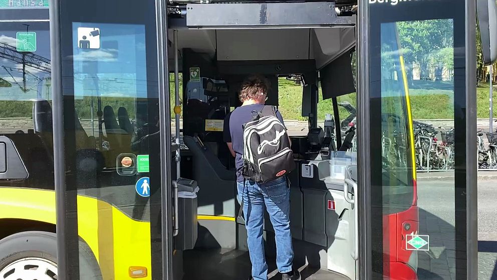 Person med ryggsäck kliver på en stadsbuss genom framdörren och visar biljett.