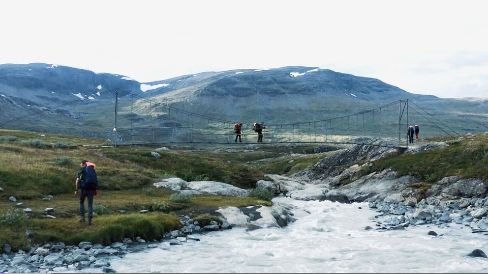 fjällvandrare som passerar en strid fors över en bro