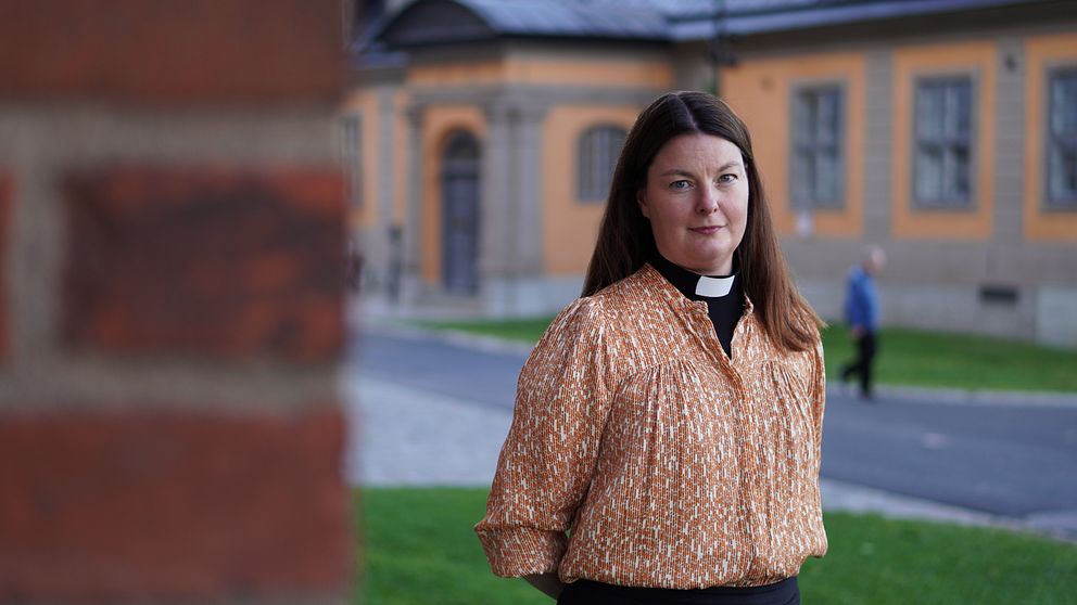 En domprost står intill domkyrkan i Uppsala, framför en gul byggnad.