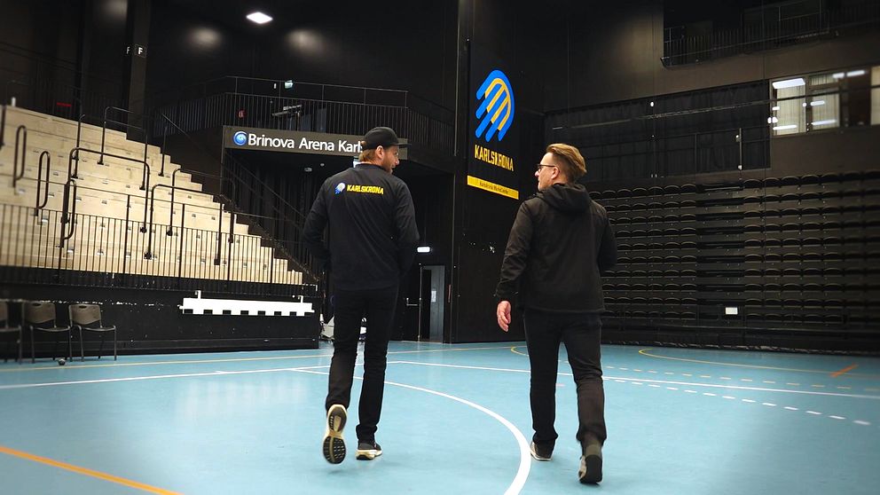HF Karlskronas klubbchef Olof Ljungberg och reporter Henrik Friberg går på en tom handbollsplan i Brinova arena.