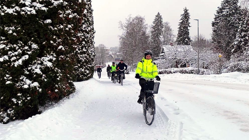 Cykelväg med snö och en kö av cyklister som cyklar mot kameran.