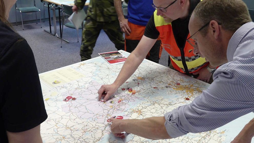 Personer i varselväst och kostym pekar på en karta över Västmanland.