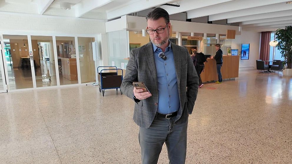 Man i kostym står i en hotellobby och tittar på sin mobiltelefon.