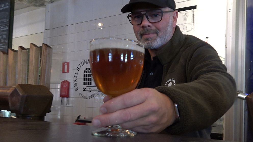 En man håller fram ett glas öl.