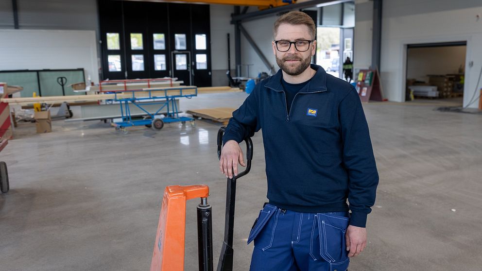 Tom Dalhqvist i arbetskläder står vid en pallvagn i en ljus industrilokal.