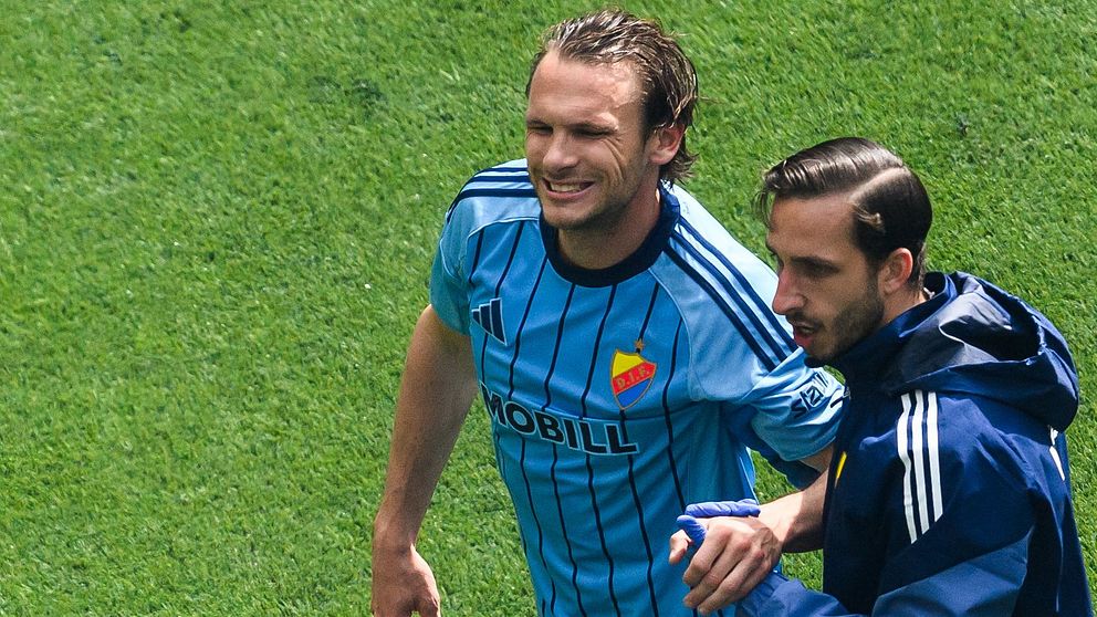 En skadad fotbollsspelare leds av planen av tre lagkamrater i träningskläder.