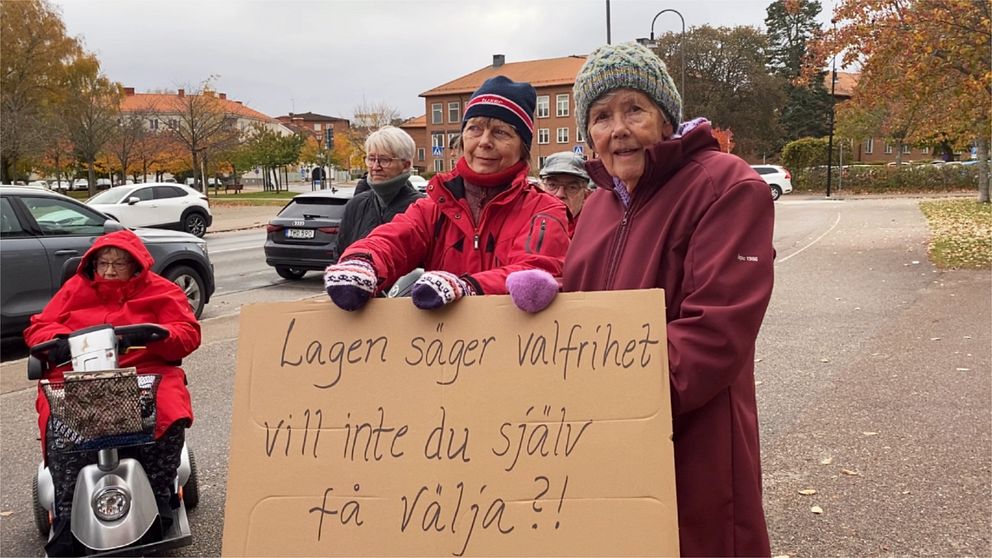 Två demonstranter utanför Strängnäs kommunhus håller i ett plakat med texten ”Lagen säger valfrihet – vill inte du själv få välja?!