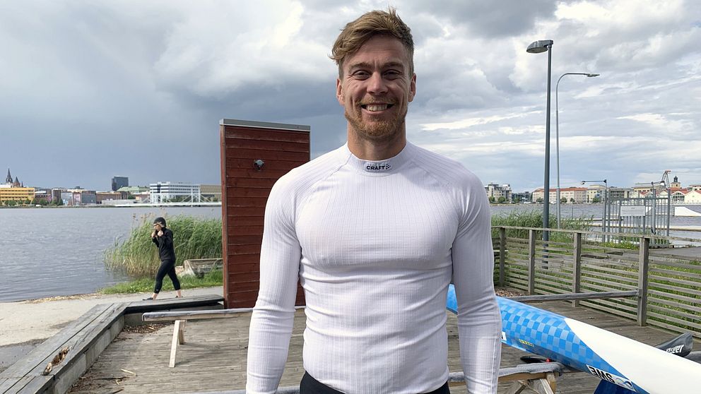 Martin Nathell står framför Munksjön, bakom honom ligger en blåvit kanot. Han har en vit långärmad tröja på sig.