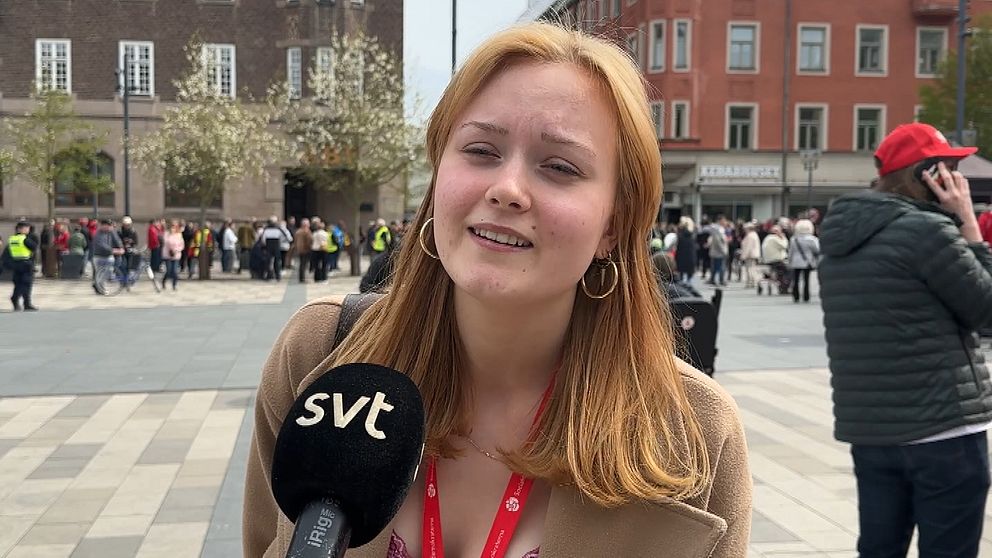 Reporter med SVT-mikrofon intervjuas på ett torg med folkmassa i bakgrunden.