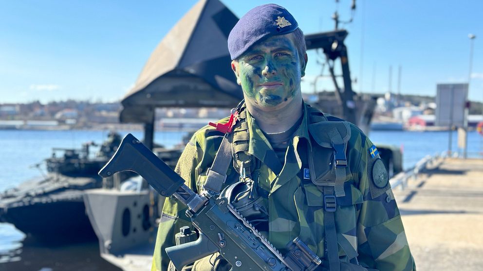 Jesper Sjögren från Sundsvall står på kajen i Härnösand i grön militäruniform, basker och kamouflagemålat ansikte. Han gör lumpen på Stockholms amfibieregemente.