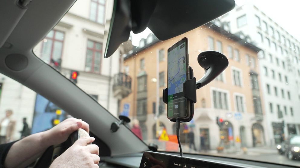 Bild på en telefon i ett bilfönster som taxiförare använder vid apptaxiresor