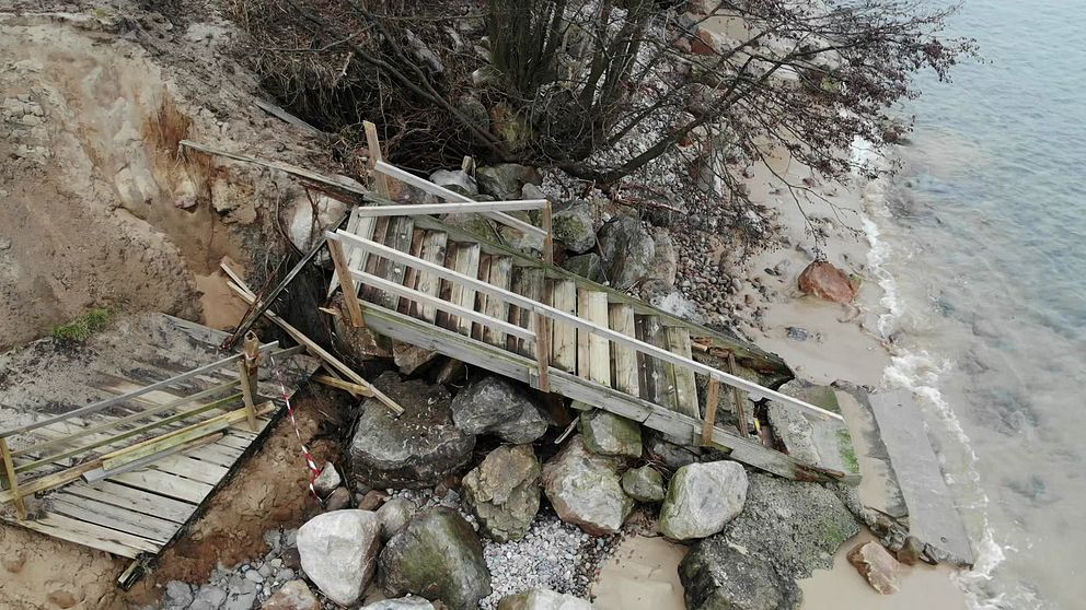 Raserad trätrappa och stenbumlingar vid vattenbrynet