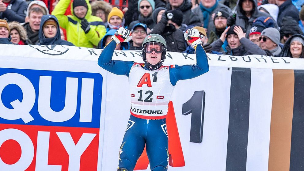En alpinskidåkare står med segergester framför en folkmassa vid tävlingsområdet, med synlig reklamskylt för ”Liqui Moly” i bakgrunden.