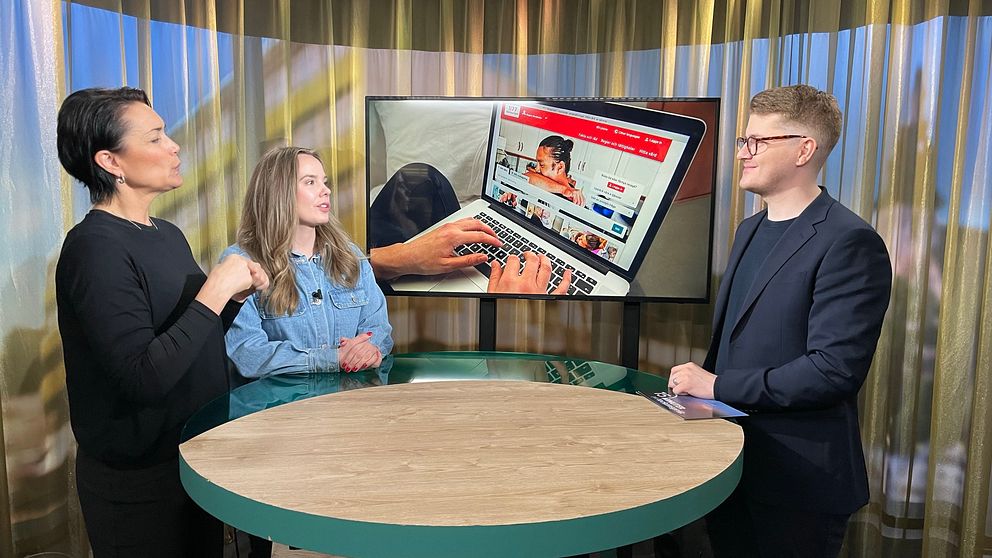 gästen står tillsammans med en tolk i studion och pratar med programledaren. I skärmen bakom studiobordet syns en person som använder 1177.se på en bärbar dator.