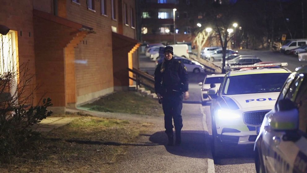 Polis går på trottoaren och flera polisbilar parkerade bredvid.