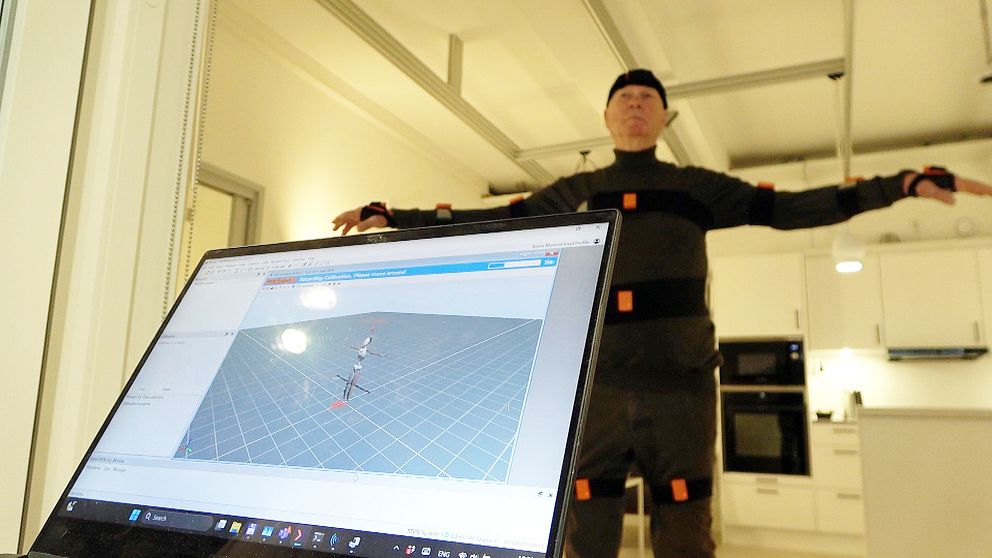 Person i motion capture-dräkt framför dator med animationsprogram.