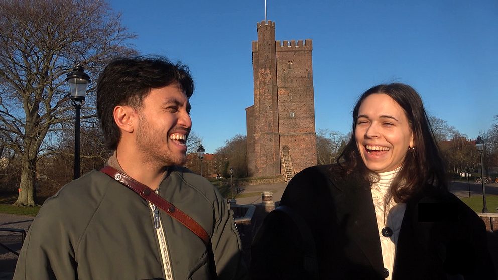 Två personer, en man och en kvinna, står framför Kärnan i Helsingborg. De skrattar och ler mot varandra.