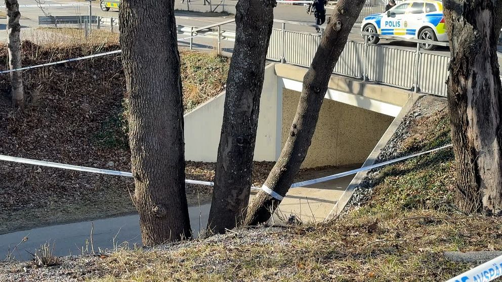 Polisbil vid avspärrat område med gångväg och bro, omgiven av träd i Geneta i Södertälje.