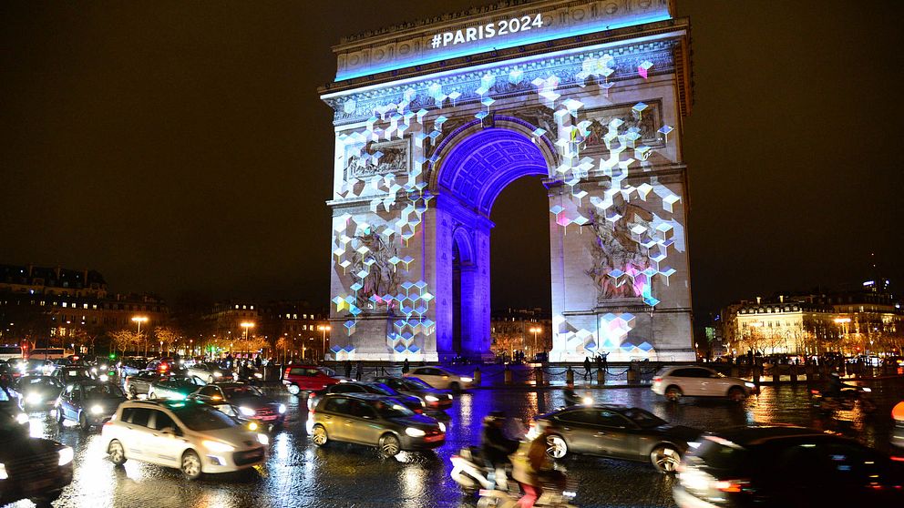 Triumfbågen i Paris, upplyst med OS-loggan och bilar nedanför.
